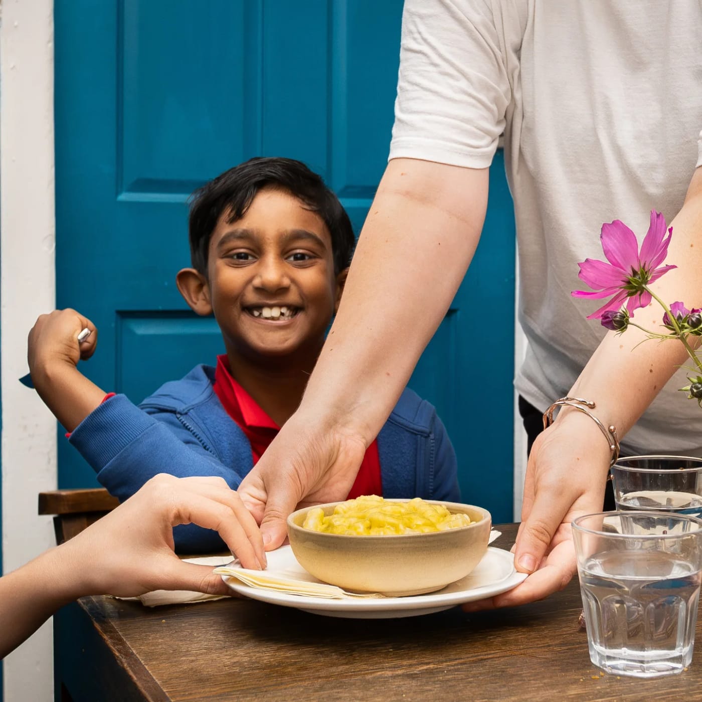 A young guest grinning as a bowl is set down in front of him at the blue door
