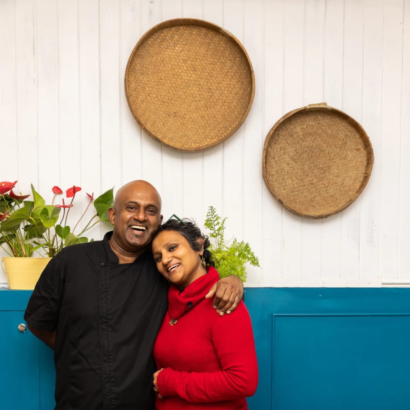 Dhayalan and Saritha laughing together outside the blue door of The Pukka Peacock